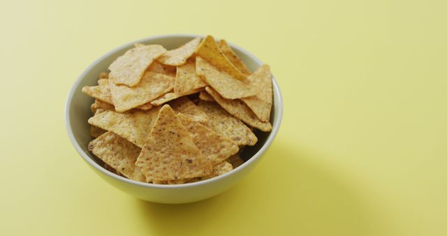 Displaying a bowl filled with freshly-made tortilla chips set against a vibrant yellow background. Ideal for advertising food products, snacking promotions, healthy snacks, or as complementary imagery for blog posts about appetizers or party foods.