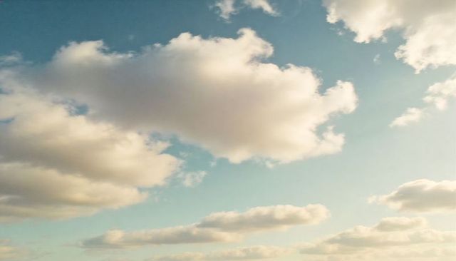 Drifting sunlit cumulus cloudscape over pale blue sky with low horizon, serene minimalism