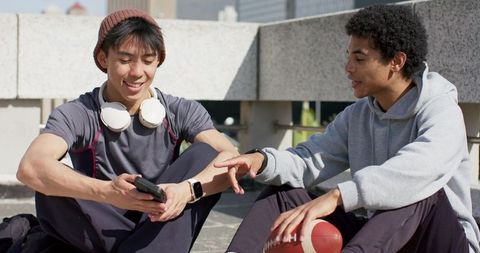 Young friends sharing music and football while relaxing on sunlit urban rooftop terrace