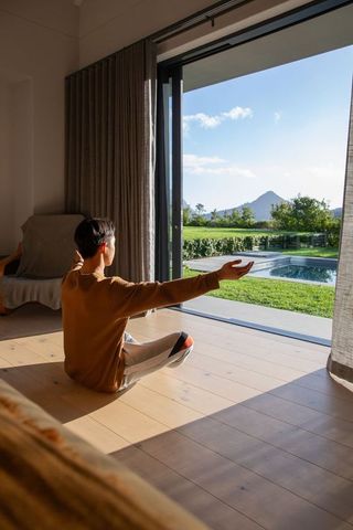 Young person sitting by open sliding glass door soaking sunlight with pool and mountain view