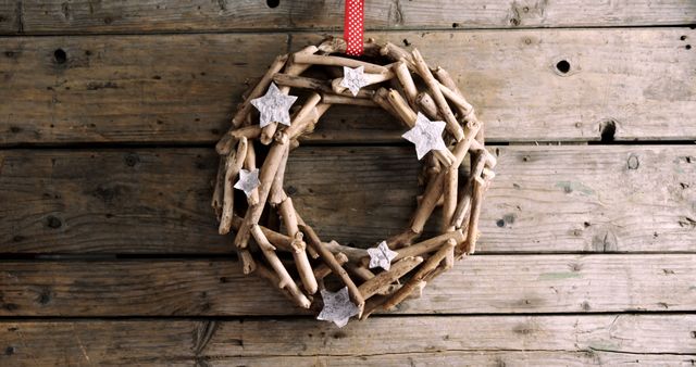 A rustic wooden wreath adorned with stars hangs on a textured wooden background, with copy space. Its natural materials and simple design convey a cozy, handmade aesthetic ideal for seasonal decor.
