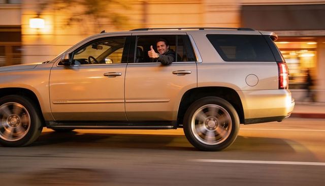 Driver giving thumbs-up from moving silver suv on city street at night