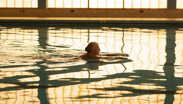 Senior woman gliding through indoor pool at golden hour, serene lap swimming wellness
