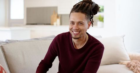 Smiling African American man on beige sofa in modern open-plan living room