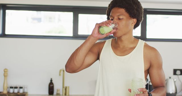 Man enjoying a nutritious green smoothie in a modern kitchen with natural light. Ideal for use in health and wellness articles, fitness blogs, healthy eating promotion, and lifestyle magazines.