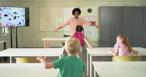 African american teacher welcoming elementary students with open arms in bright classroom