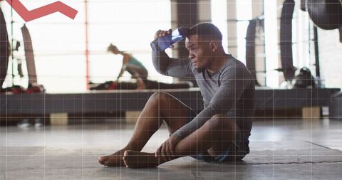 Exhausted athlete sitting on gym floor cooling with water bottle after intense workout