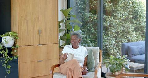 Senior african woman sipping coffee in cozy sunlit lounge with houseplants