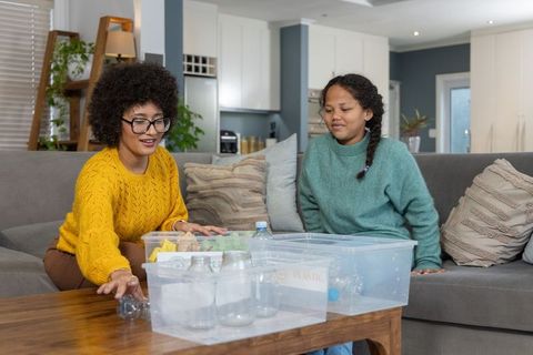 Mother and daughter testing plastic bottles in water tubs on sofa for recycling experiment