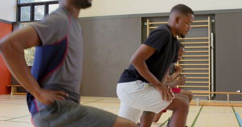 African american men doing dynamic warmup lunges on gym court for team fitness