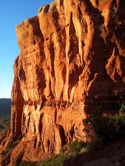 Beautiful vertical sunlit red rock cliff capturing the rugged beauty of Arizona's desert landscape, ideal for travel and adventure themes, nature and geological studies, and promoting outdoor activities in the American Southwest.