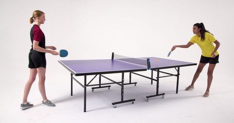 Two female friends competing in ping-pong in studio setting