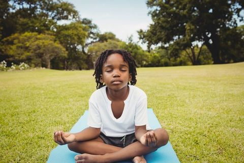 Young boy meditating outdoors on blue yoga mat in tranquil field