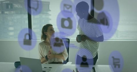 Female colleagues collaborating in modern office reviewing documents with digital icons