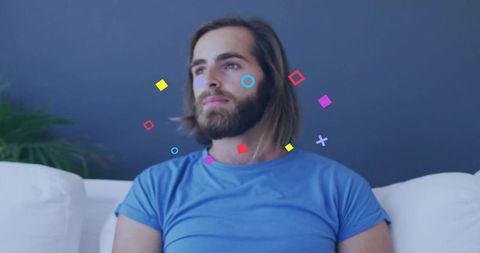 Bearded man gazing while colorful geometric shapes floating around head on modern couch