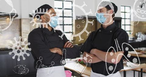 Two chefs wearing masks crossing arms in commercial kitchen promoting hygiene and teamwork