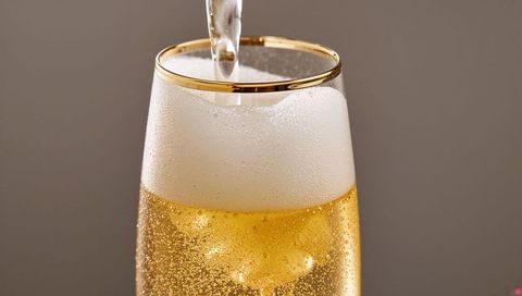 Pouring champagne into gold-rimmed flute showing effervescent bubbles and foam