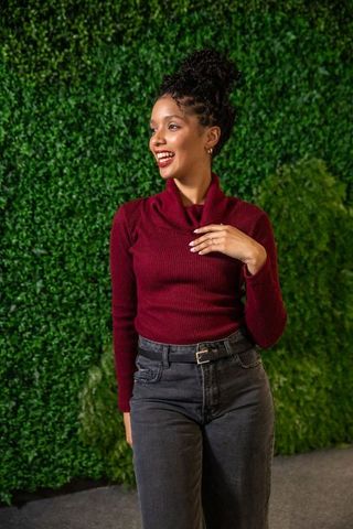 African american woman smiling in burgundy sweater against green foliage wall, portrait