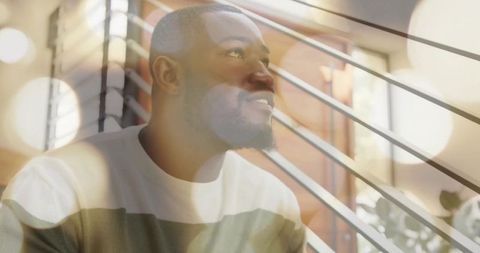 Gazing man sitting by window slats with warm bokeh and lensflare, closeup portrait