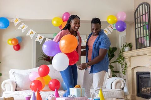 African american couple arranging colorful party balloons and gifts in living room