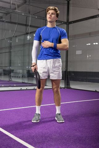 Young athlete standing on purple court holding paddle wearing blue shirt and arm sleeve