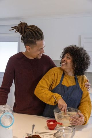 African american couple baking together in cozy sunlit kitchen, stirring batter, smiling