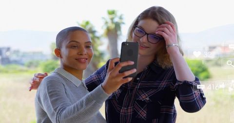 Cheerful friends capturing moments with smartphone outdoors