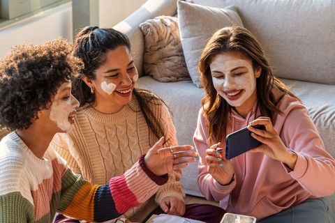 Multicultural friends having at-home spa night applying face masks laughing together