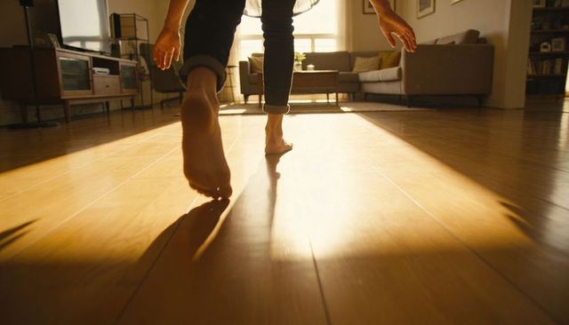 Barefoot walking across sunlit hardwood floor in minimalist living room