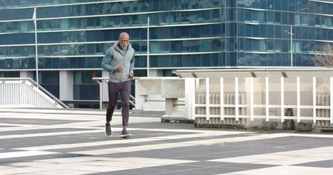Senior african american man jogging on urban plaza with modern glass building backdrop