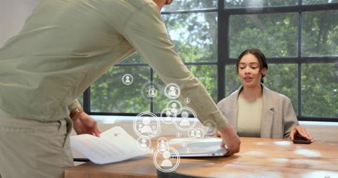 Businesswoman reviewing documents while colleague preparing laptop for team meeting