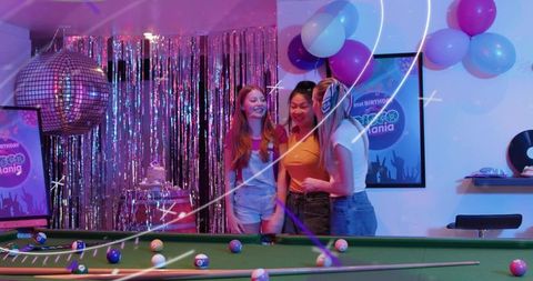 Smiling friends celebrating retro disco birthday at pool table with mirrorball balloons