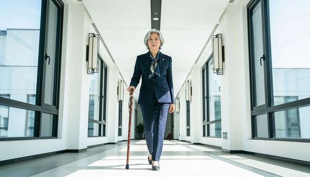 Confident senior asian woman walking with ornate cane in modern office corridor