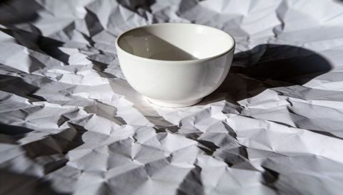 White porcelain bowl casting dramatic shadow on crumpled paper texture minimalist