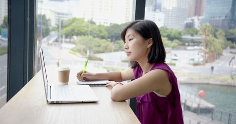 Businesswoman Writing Notes on Laptop in Modern Office