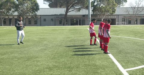 Soccer Team Celebrating Goal on Sunny Field with Enthusiastic Coach