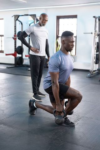 African american trainer guiding male trainee performing kettlebell lunges to build strength