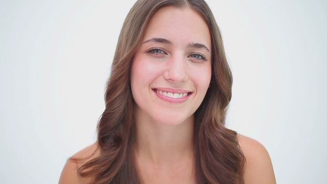 Woman with brown hair smiling and massaging her cheek with a soft expression. Skin appears healthy and glowing, suggesting a moment of relaxation and self-care. Useful for wellness promotions, skincare tutorials, beauty care products advertising, and modern lifestyle content.