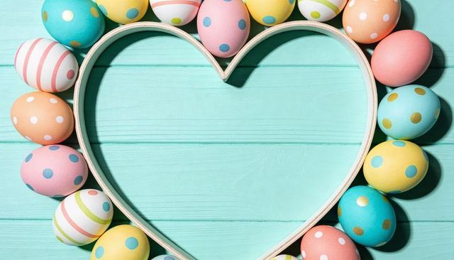 Framing pastel easter eggs with heart-shaped wooden frame on turquoise planks