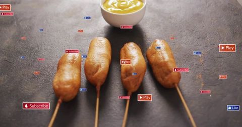 Golden crispy corn dogs on skewers with mustard bowl and play subscribe media badges