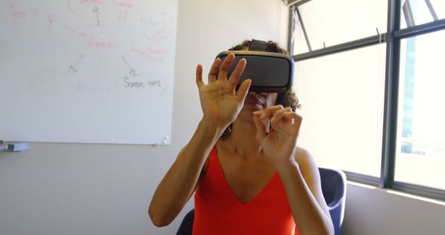 Woman wearing VR headset while using hand gestures in a modern office environment. Ideal for showcasing technological advancements, virtual reality training, innovative workspace setups, or interactive simulation experiences.