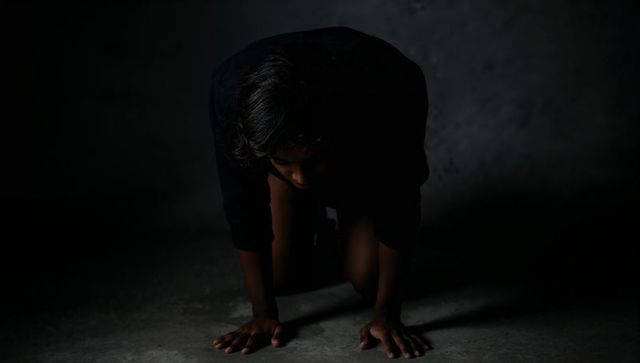 Solitary figure kneeling on floor under dramatic lamp light creating moody chiaroscuro