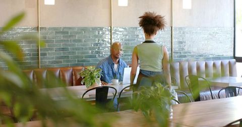 African american man and woman collaborating in modern cafe with laptop and plants