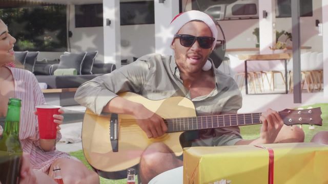 Diverse group of friends celebrates Christmas outdoors in sunny weather, singing, playing guitar, and drinking beer. Perfect for content related to multicultural holiday celebrations, American patriotism, summer events, and festive gatherings.