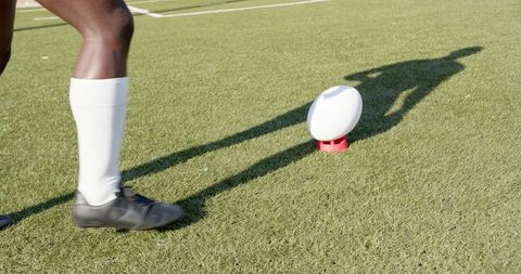 Athlete prepares for rugby kick on field with shadow