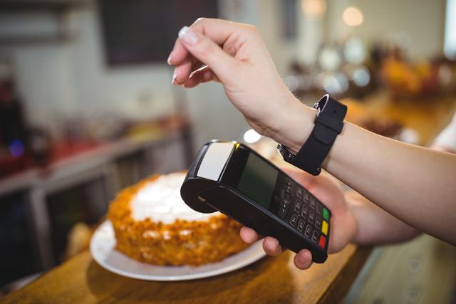 Woman using smartwatch to make a contactless payment in a cafe. Ideal for illustrating modern technology, digital wallets, and convenience in everyday transactions. Useful for articles or advertisements related to fintech, smart devices, and customer service in the food and beverage industry.