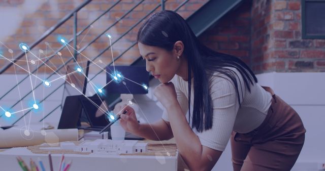 A female architect is concentrating on analyzing a 3D building model using advanced virtual technology. This image can be used for topics related to architectural design, innovative technology in construction, modern professional environments, women's roles in engineering and architecture, and virtual reality interfaces.