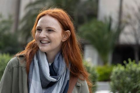 Redhead woman smiling in urban courtyard wearing scarf and olive jacket, candid portrait