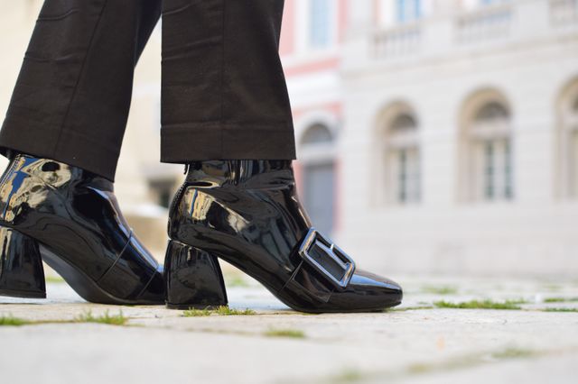 Close-up of fashionable black patent leather boots with buckle detail in urban setting. Perfect for shoe advertisements, fashion blogs, urban lifestyle features, and social media posts showcasing trendy footwear.