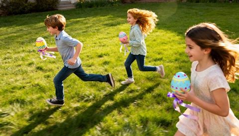 Three children running with pastel easter eggs across sunlit backyard lawn, spring fun